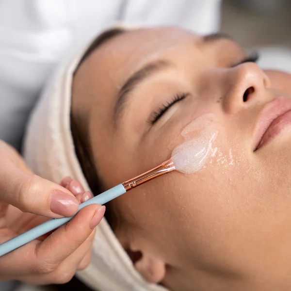A woman receiving a facial treatment, applying a blue brush to her skin for skincare enhancement.